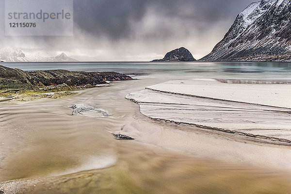 Eine Landschaft mit zerklüfteten Bergen und Sand entlang der Küstenlinie unter einem bewölkten Himmel; Nordland  Norwegen