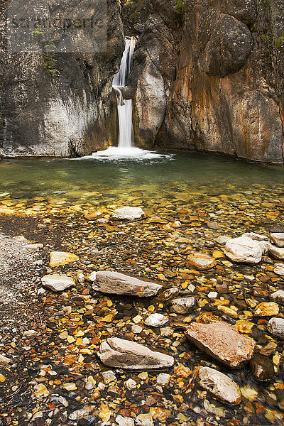 Ein doppelter Wasserfall zwischen dunklen Felswänden mit bunten kleinen Felsen und Kieselsteinen im Vordergrund; Calgary  Alberta  Kanada