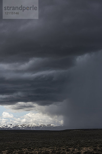 Dramatische Gewitterwolke über einem offenen Feld mit einer schneebedeckten Bergkette in der Ferne; Idaho  Vereinigte Staaten von Amerika
