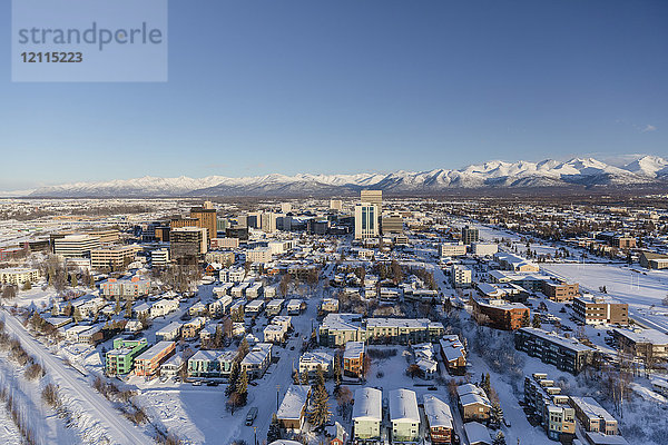 Luftaufnahme der schneebedeckten Innenstadt von Anchorage und der Chugach Mountains in der Ferne  im Vordergrund sind der Park Strip und das Capitan Cook Hotel zu sehen  Süd-Zentral-Alaska im Winter; Anchorage  Alaska  Vereinigte Staaten von Amerika