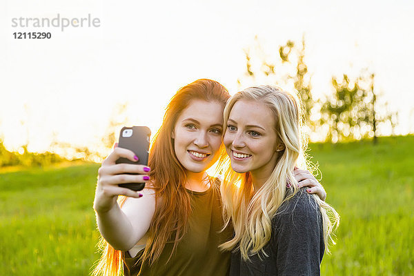 Zwei Freunde stehen in einem Park und machen ein Selbstporträt mit einem Smartphone in der Abenddämmerung; Edmonton  Alberta  Kanada