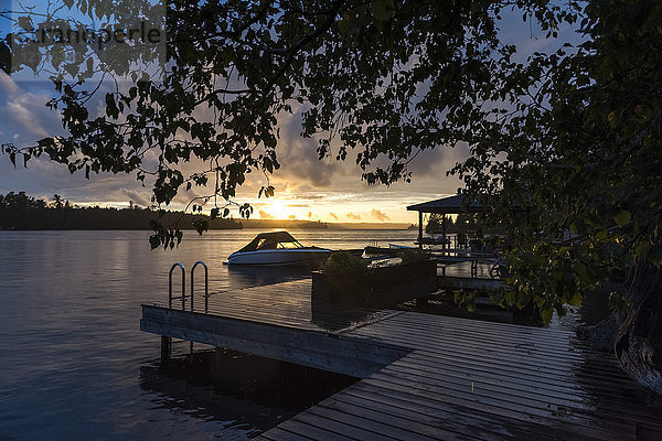 Sonnenuntergang über einem ruhigen See mit einem Steg und einem Boot im Vordergrund; Lake of the Woods  Ontario  Kanada