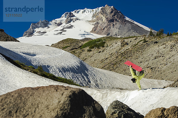 Ein professioneller Freeride-Snowboarder überschlägt sich in der Luft auf einer verschneiten Piste mit schroffen Bergspitzen; British Columbia  Kanada