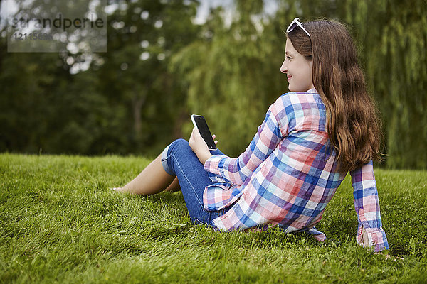 Mädchen im Teenageralter sitzt in einem Park und hält ein Tablet; Toronto  Ontario  Kanada