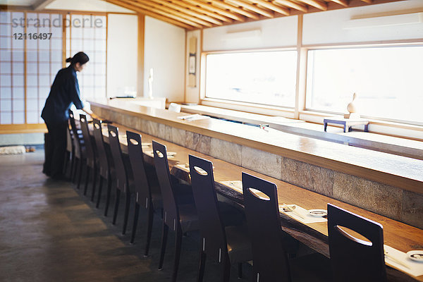 Kellnerin  die an einem Tresen in einem japanischen Sushi-Restaurant steht und Gedecke vorbereitet.