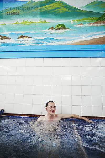 Ein junger kaukasischer Mann saß in einem tiefen Becken mit fließendem Wasser in einem öffentlichen Badehaus.
