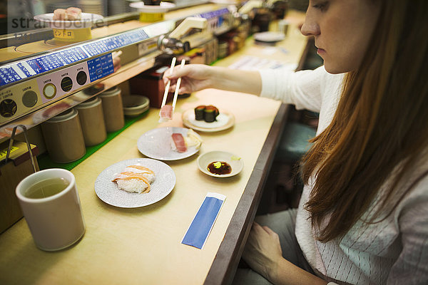 Hochwinkelaufnahme einer Frau  die in einer Sushi-Bar isst  mit Sushi-Zug  Kaiten-zushi.