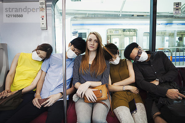 Fünf Personen mit Staubmasken  die nebeneinander in einem U-Bahn-Zug sitzen  Pendler aus Tokio.