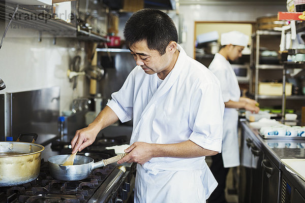 Koch  der in der Küche eines japanischen Sushi-Restaurants arbeitet und auf dem Herd kocht.
