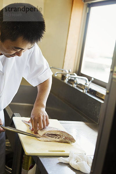 Chefkoch  der an der Theke eines japanischen Sushi-Restaurants arbeitet und Fischfilet in Scheiben schneidet.