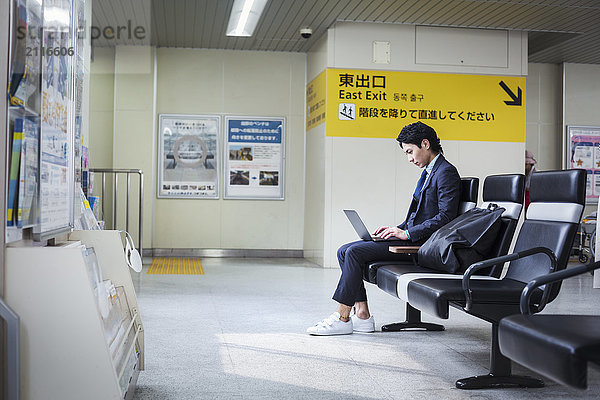 Geschäftsmann im Anzug  der am Bahnhof sitzt und am Laptop arbeitet.