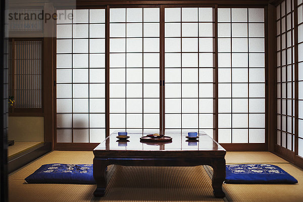 Traditionelles japanisches Interieur mit niedrigem  mit Teeschalen gedecktem Tisch.