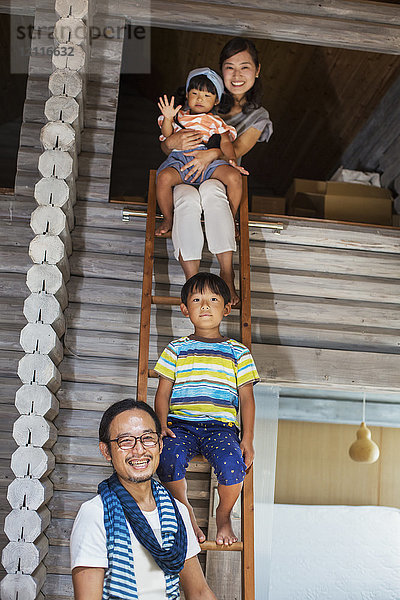 Familie  Mann  Frau  Junge und junges Mädchen sitzen auf einer Leiter und lächeln in die Kamera.