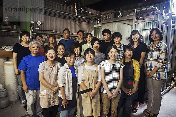 Gruppenporträt der Mitarbeiter einer japanischen Porzellanwerkstatt  die vor dem Ofen stehen und in die Kamera lächeln.