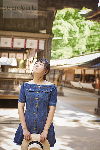 Junge Frau in blauem Kleid und mit Hut in der Hand am Shinto Sakurai-Schrein  Fukuoka  Japan.