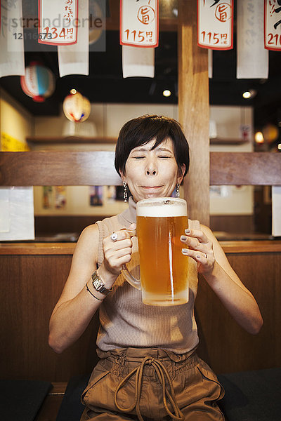 Frau  die an einem Tisch in einem Restaurant sitzt und ein großes Glas Bier hält.
