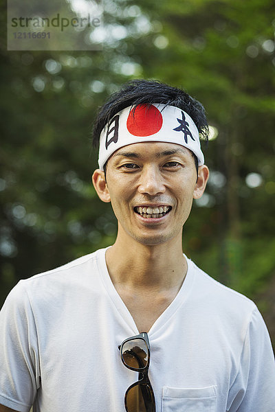Porträt eines Mannes mit Stirnband und japanischer Flagge  der in die Kamera lächelt.