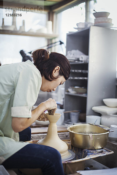 Frau  die in einer japanischen Porzellanwerkstatt arbeitet  an einer Töpferscheibe sitzt und Schüssel wirft.