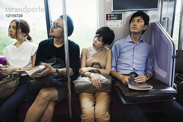 Vier Menschen sitzen nebeneinander in einem U-Bahn-Zug  Tokio-Pendler.