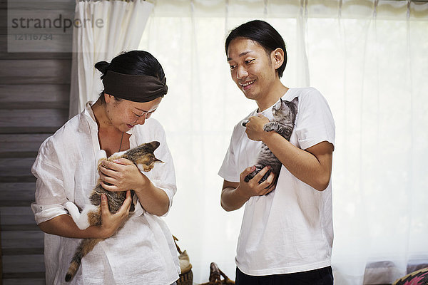 Mann und Frau stehen im Haus und halten jeweils eine Kattunkatze mit weißem  schwarzem und braunem Fell.