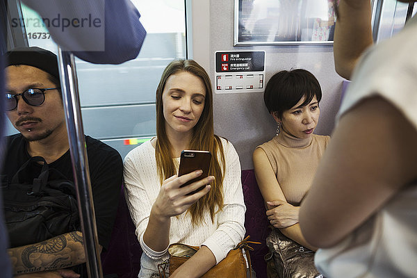 Drei Menschen sitzen nebeneinander in einem U-Bahn-Zug  Pendler aus Tokio.