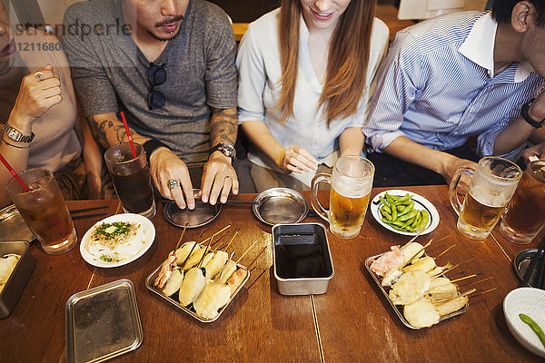 Hochwinkelaufnahme von fünf Personen  die nebeneinander an einem Restauranttisch mit Speisen und Getränken sitzen.