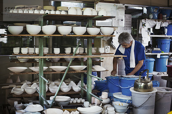 Mann steht in einer japanischen Porzellanwerkstatt mit Regalen verschiedener Porzellanschalen.