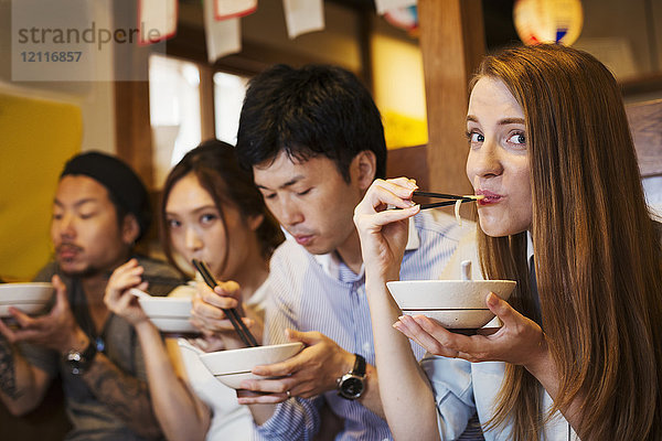 Vier Personen sitzen nebeneinander an einem Tisch in einem Restaurant und essen mit Stäbchen aus Schalen.