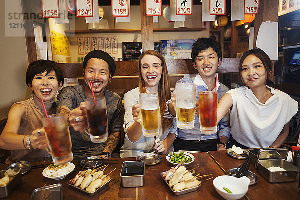 Fünf Personen sitzen nebeneinander an einem Tisch in einem Restaurant und halten große Gläser mit Erfrischungsgetränken und Bier in der Hand.