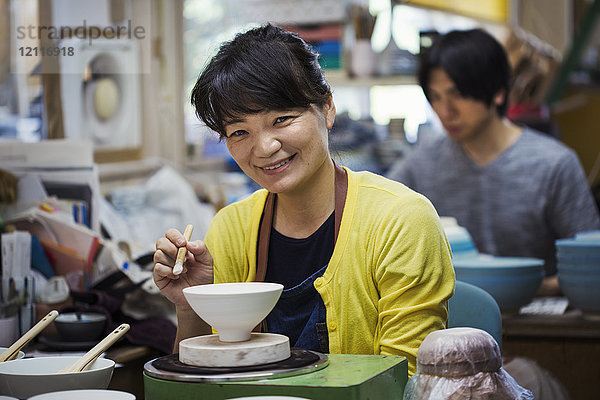 Lächelnde Frau und Mann sitzen in einer Werkstatt und arbeiten an japanischen Porzellanschüsseln.