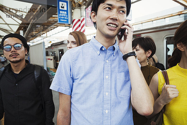Kleine Gruppe von Menschen  die auf dem Bahnsteig einer U-Bahn-Station stehen  Pendler aus Tokio  Mann mit Smartphone.