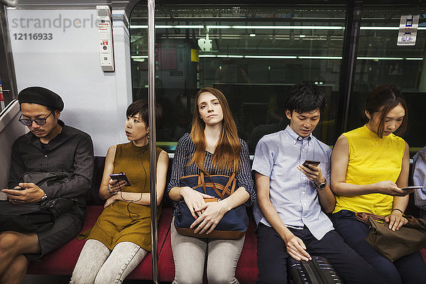 Fünf Menschen sitzen nebeneinander in einem U-Bahn-Zug  Tokio-Pendler.