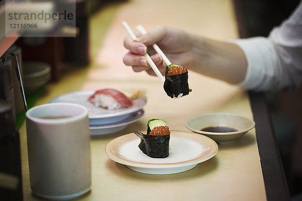 Nahaufnahme einer Person  die in einer Sushi-Bar isst  mit Sushi-Zug  Kaiten-zushi.