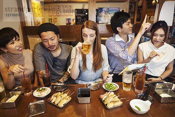 Fünf Personen sitzen nebeneinander an einem Tisch in einem Restaurant  essen und trinken Bier.