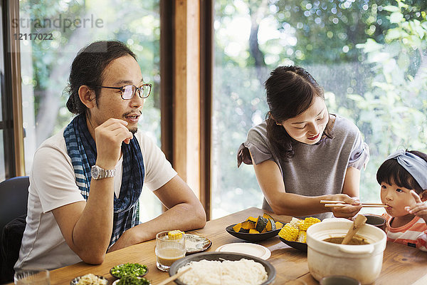 Mann  Frau und junges Mädchen sitzen an einem Tisch mit Schüsseln mit Essen und essen gemeinsam.