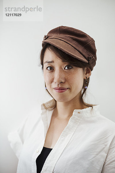 Frau mit weißem Hemd und brauner Mütze steht in der Kunstgalerie und lächelt in die Kamera.