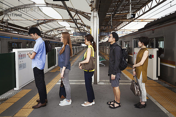 Fünf Menschen stehen in einer Reihe auf einem U-Bahn-Bahnsteig und warten in der Schlange  Tokio-Pendler.