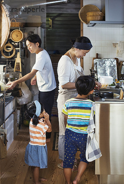 Mann  Frau mit Schürze  Junge und junges Mädchen stehen in einer Küche und bereiten Essen vor.