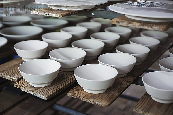 Hochwinkel-Nahaufnahme von weißen Schalen und Tellern in einer japanischen Porzellanwerkstatt.