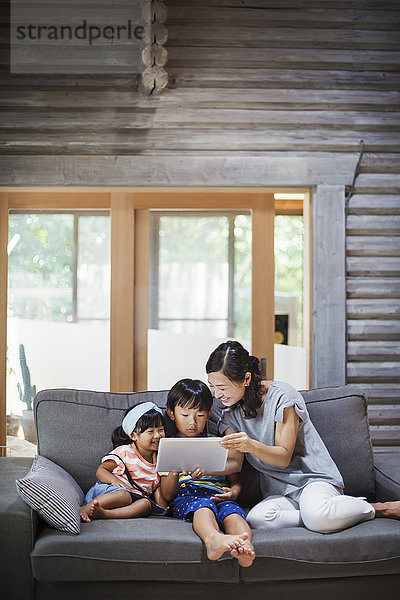 Frau  Junge und junges Mädchen sitzen auf einem grauen Sofa und schauen auf ein digitales Tablett.