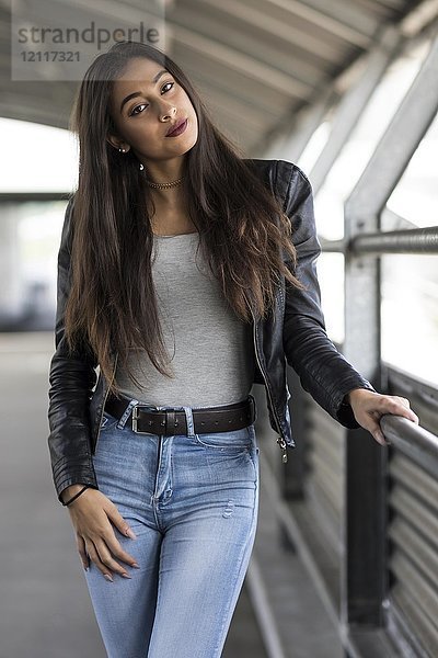 Junge Frau mit langen braunen Haaren in Jeans und Lederjacke