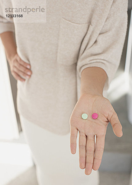 Frau hält zwei Pillen in der Hand  rosa und grün