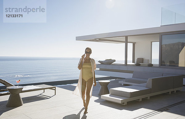 Frau im Badeanzug  die auf einer sonnigen  modernen  luxuriösen Musterhaus-Terrasse mit Meerblick spazieren geht