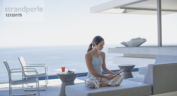Frau im Schlafanzug mit digitalem Tablet auf moderner  luxuriöser Haustür mit Blick aufs Meer
