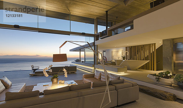 Beleuchtetes modernes Luxus-Wohnzimmer mit Meerblick in der Abenddämmerung