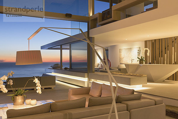 Beleuchtetes  modernes Luxus-Wohnzimmer mit Meerblick in der Abenddämmerung