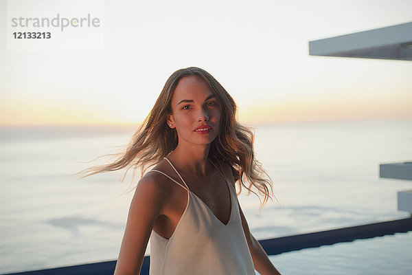 Porträt einer selbstbewussten Frau  die sich auf einem luxuriösen Balkon mit Blick auf den Sonnenuntergang dreht