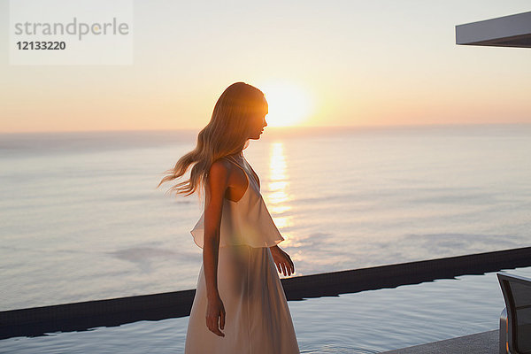 Frau im weißen Kleid auf einer ruhigen  luxuriösen Terrasse mit Blick auf das Meer bei Sonnenuntergang