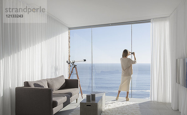 Frau mit Fotohandy fotografiert sonnigen Blick auf das Meer von modernen  luxuriösen Haus Schaufenster Innenraum Wohnzimmer