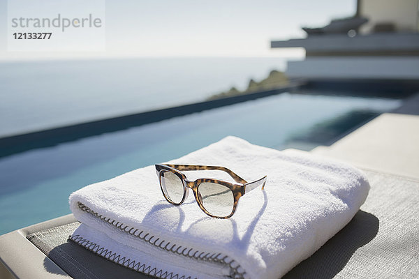 Sonnenbrille auf gefaltetem Handtuch am sonnigen Luxus-Pool